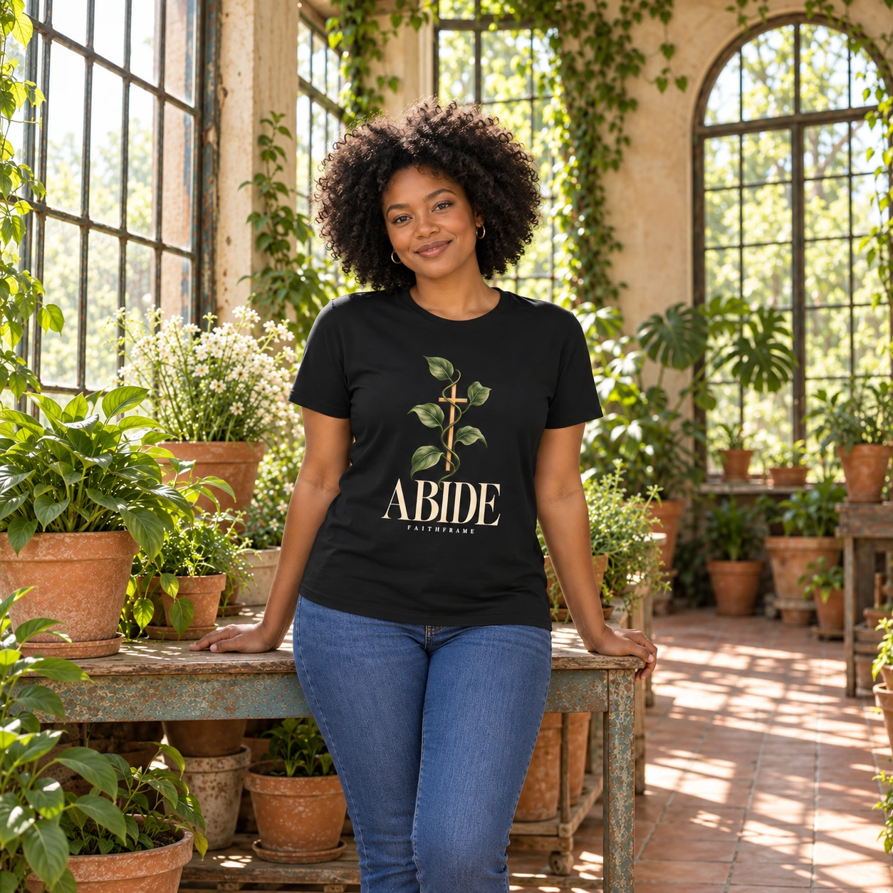 Woman wearing the black Abide tee in a sunlit plant conservatory