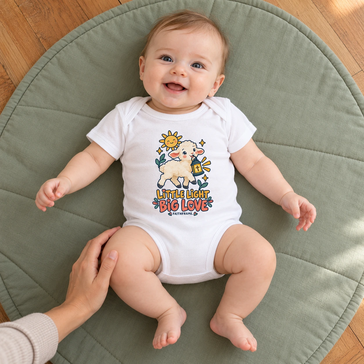 Baby wearing the white Little Light Big Love bodysuit on a floor play mat beside a caregiver